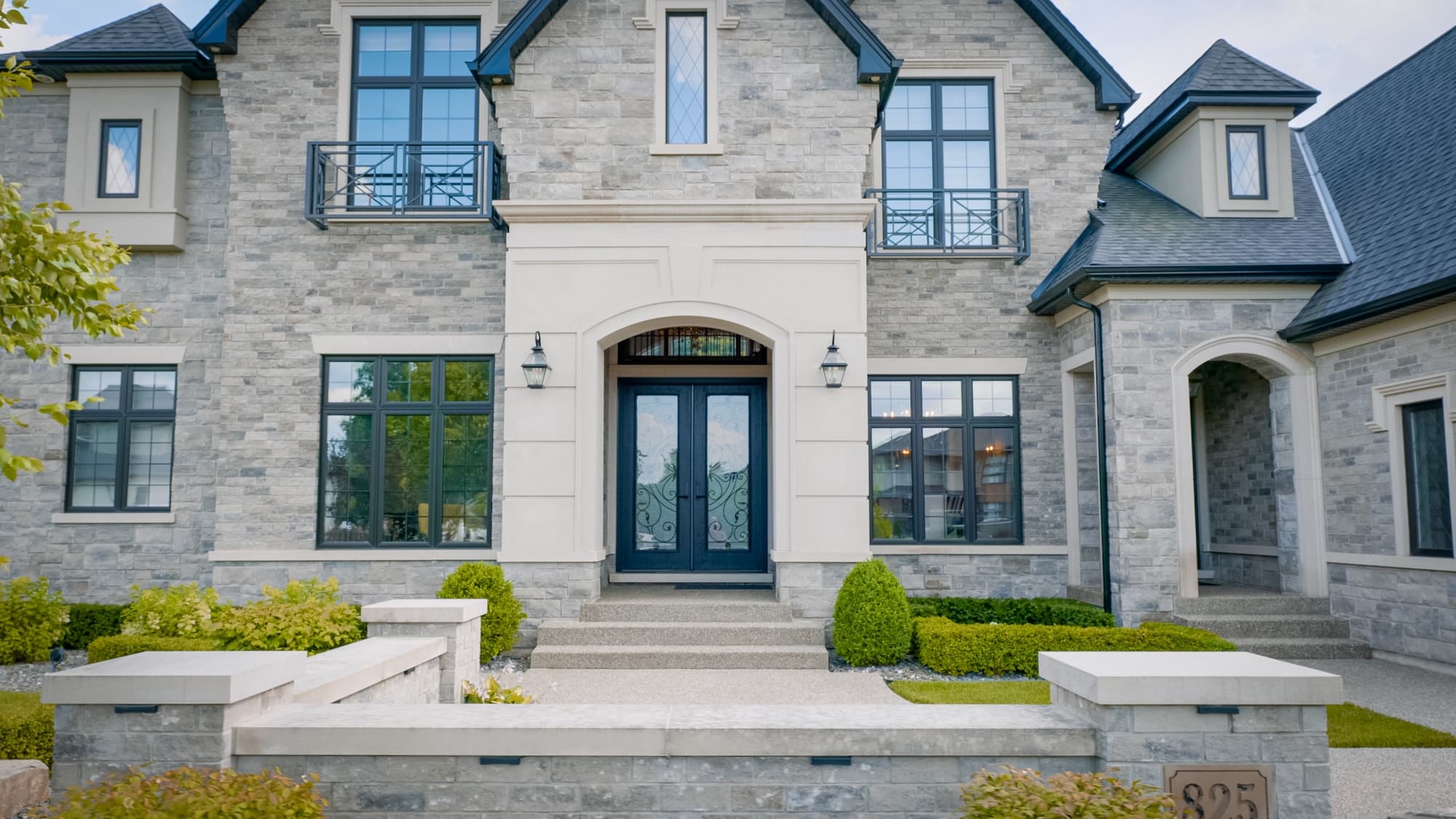 Elegant stone home entrance with iron balconies and landscaping by Timberland Homes in Chatham, Ontario.