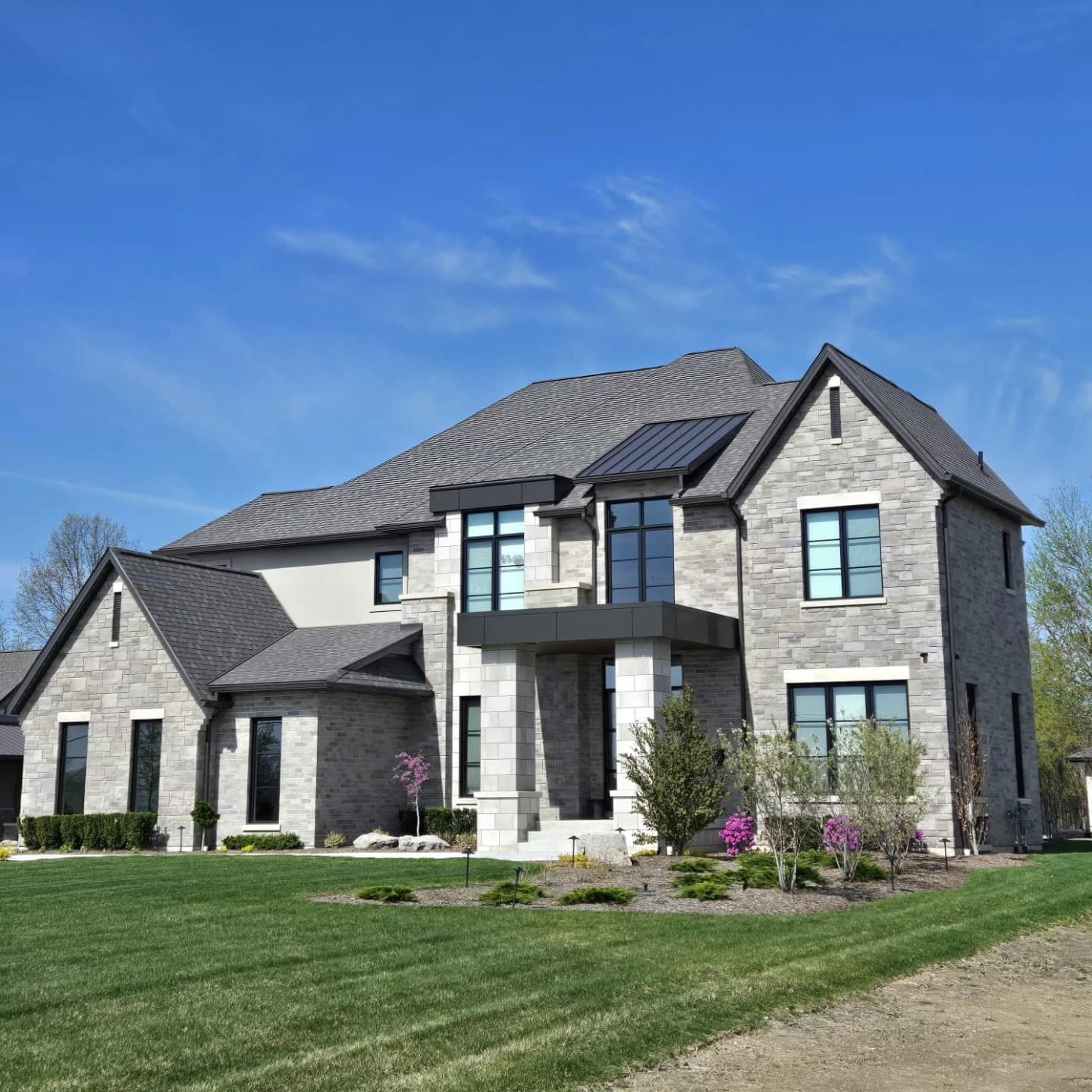 Grey stone two-story custom home with covered balcony and spring landscaping built by Timberland Homes in Kingsville, Ontario