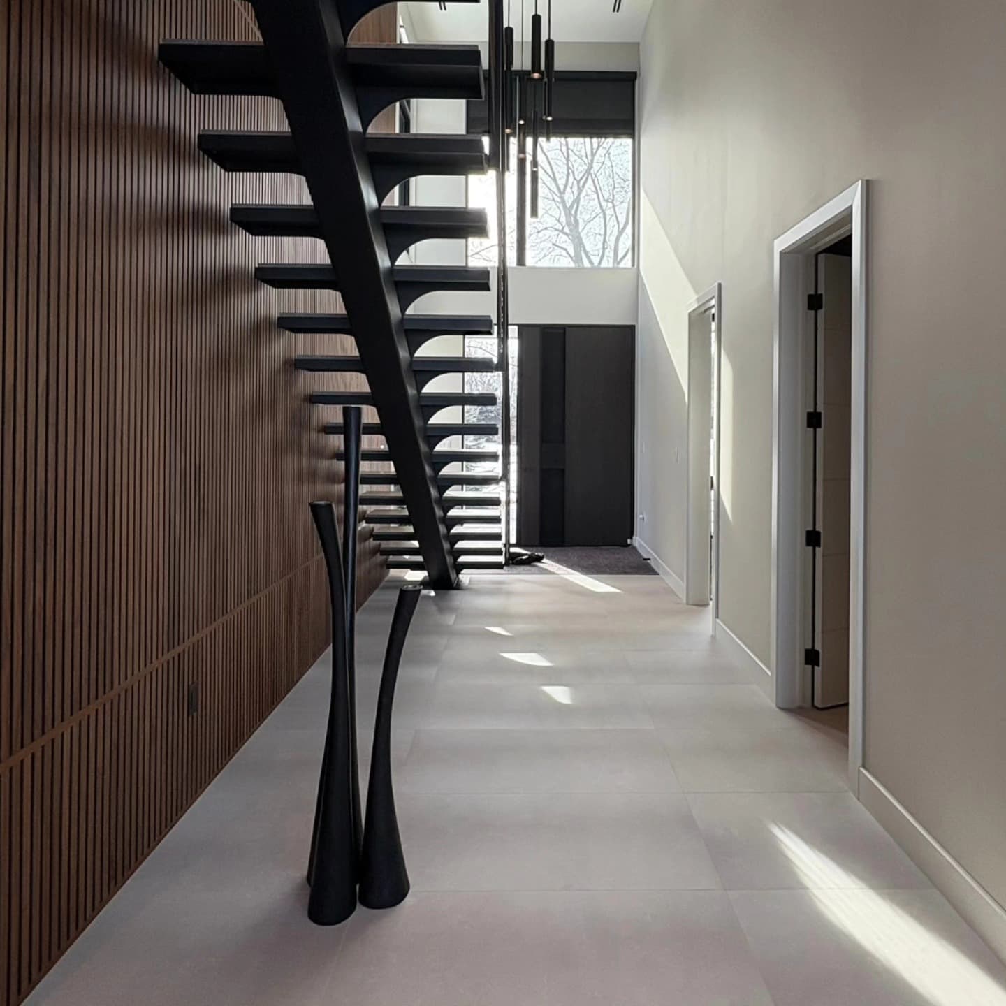 Modern entryway with sculptural floating black staircase and slatted wood accent wall in a Timberland home in Amherstburg, Ontario