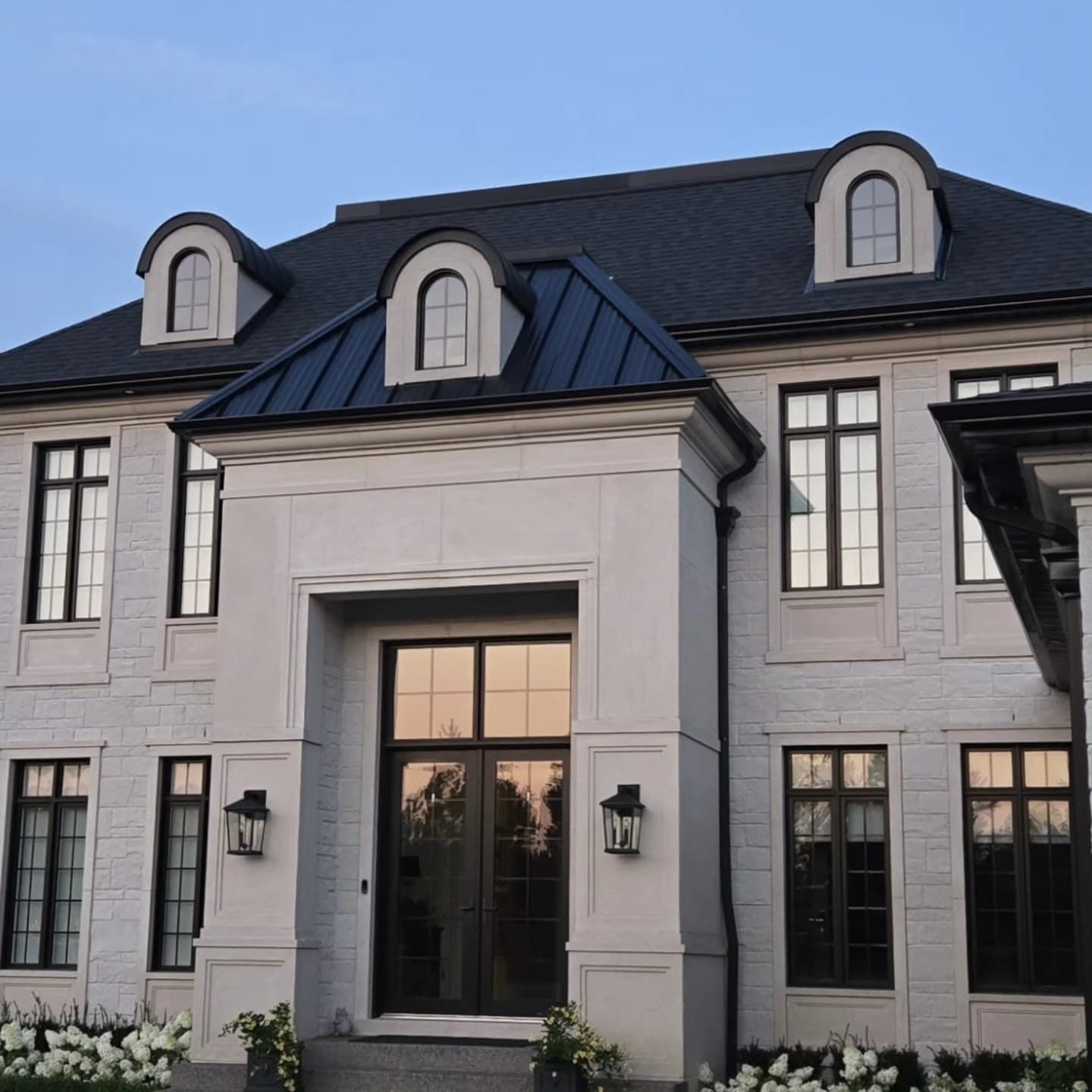French-inspired white stone custom home with arched dormers and metal roof at dusk, built by Timberland Homes in Windsor, Ontario